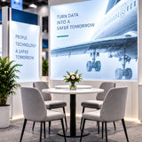 Aviation booth meeting area with gray chairs, a round table and an illuminated aircraft backdrop